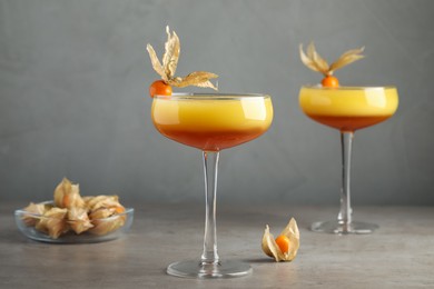 Photo of Tasty cocktail decorated with physalis fruits on grey table