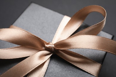 Gift box with golden bow on black background, closeup