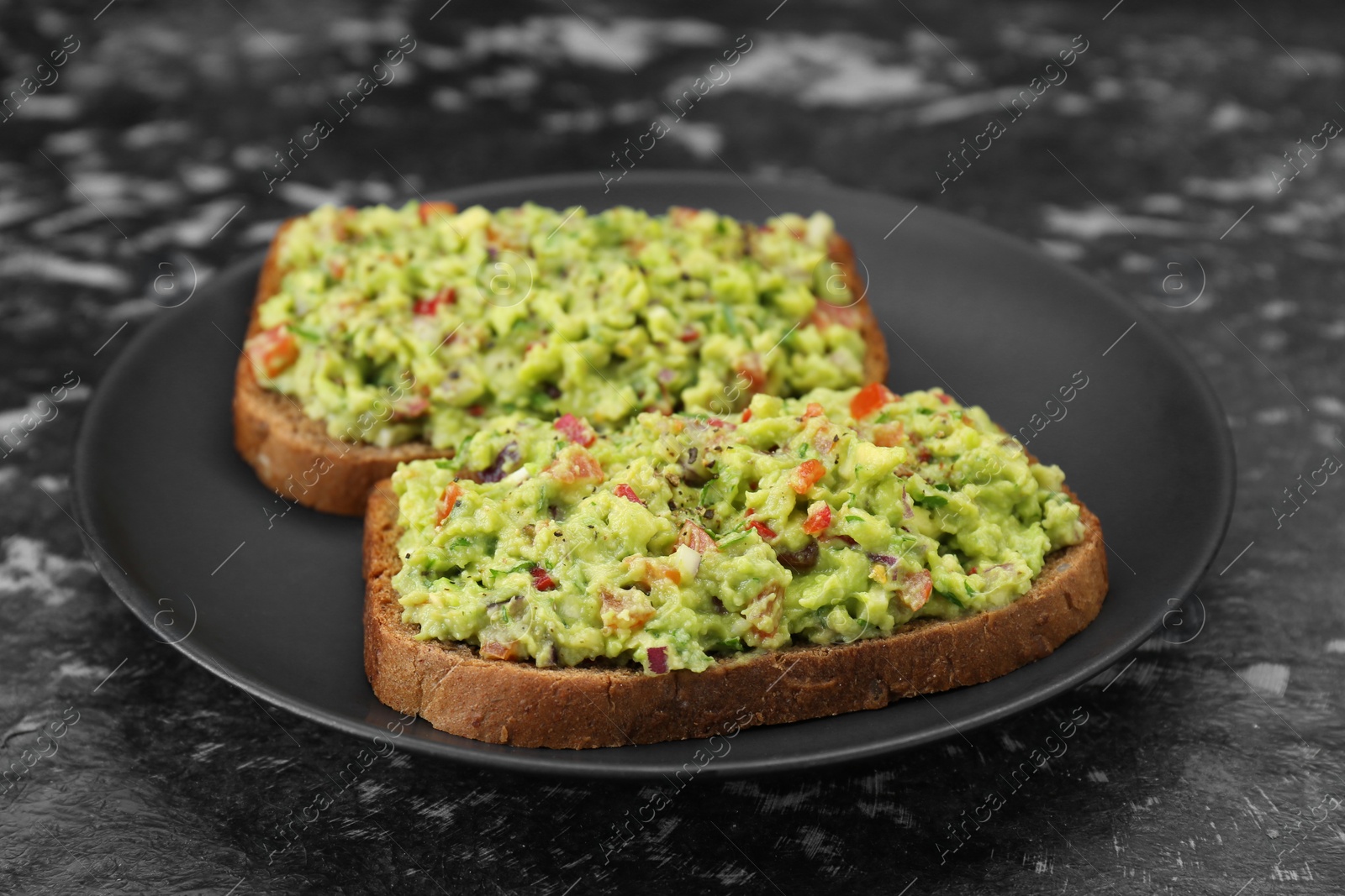 Photo of Slices of bread with tasty guacamole on black textured table, closeup