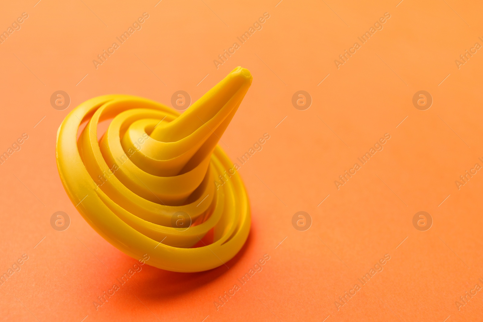 Photo of One yellow spinning top on orange background, closeup. Space for text