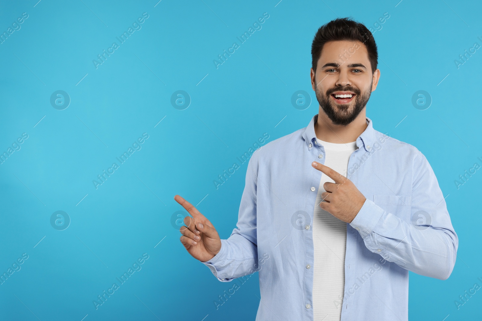 Photo of Special promotion. Smiling man pointing at something on light blue background. Space for text