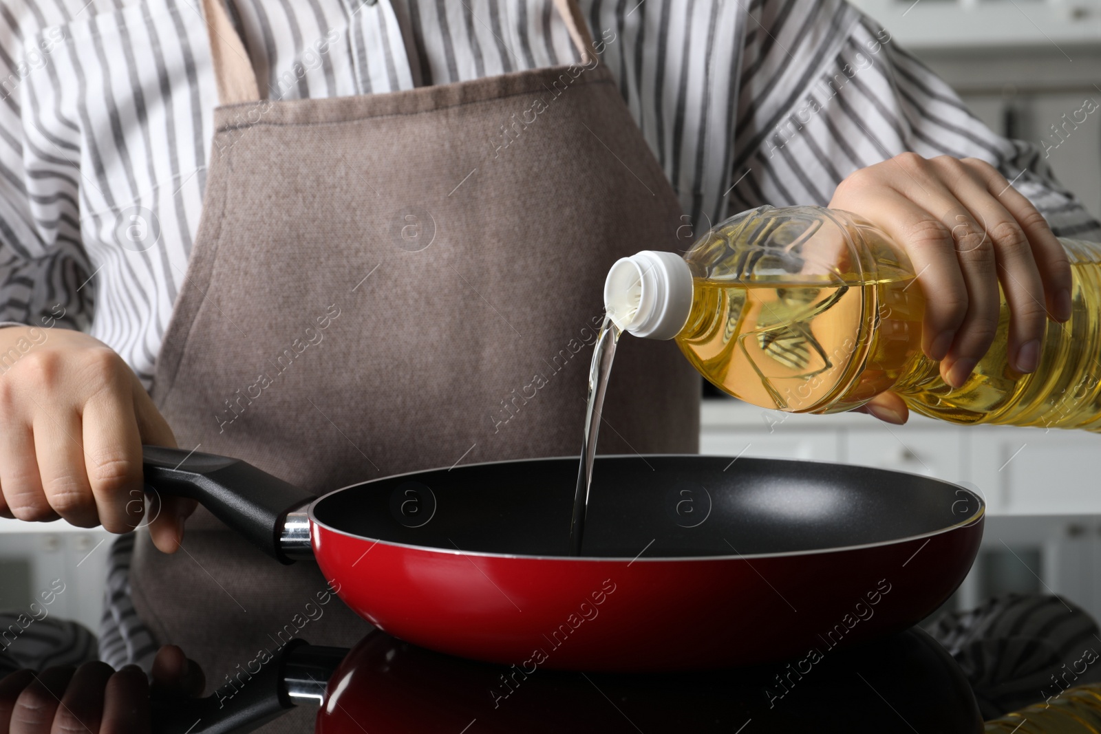 Photo of Woman pouring cooking oil from bottle into frying pan on stove, closeup