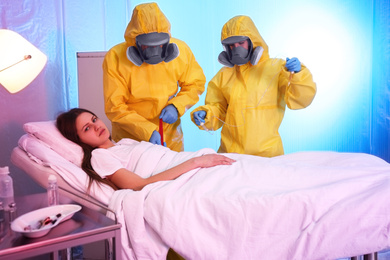Paramedics wearing protective suits examining patient with virus in quarantine ward