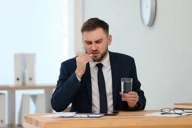Photo of Man taking pill against migraine in office