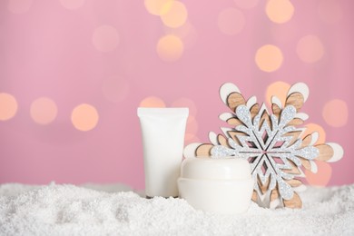 Photo of Set of winter skin care cosmetics with hand cream and decorative snowflake on snow against blurred lights. Space for text