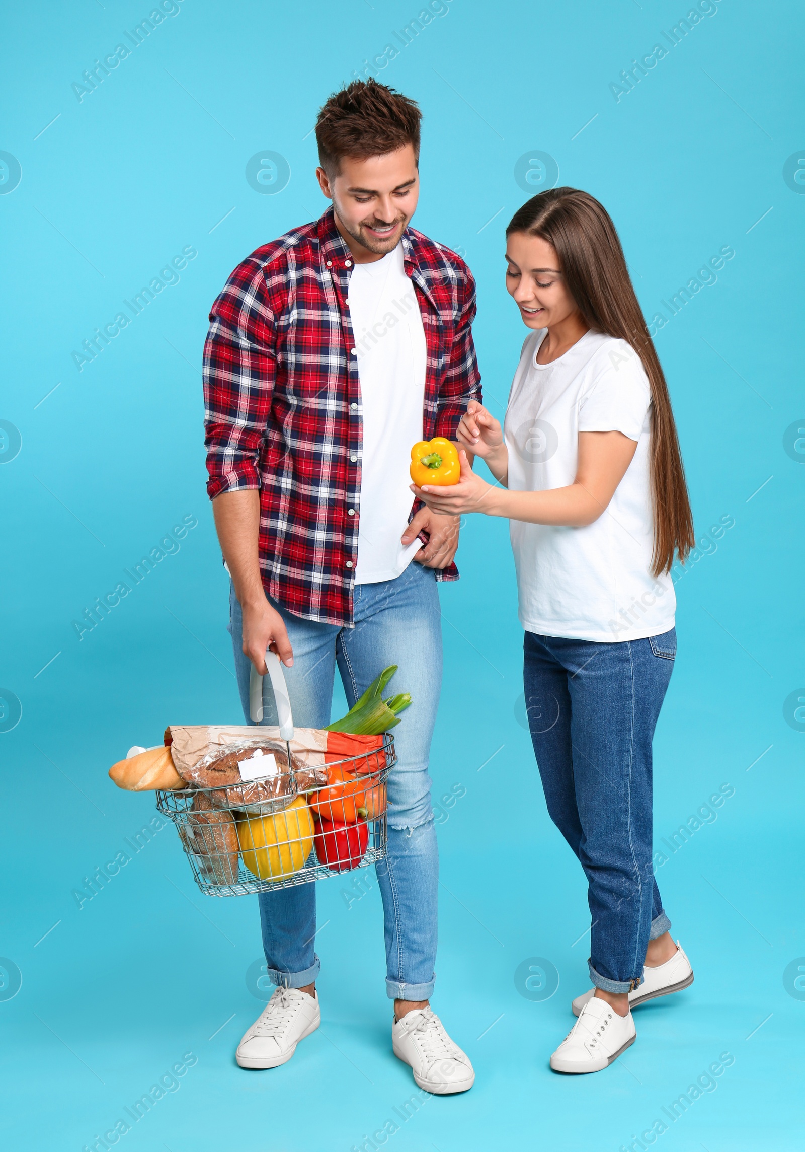 Photo of Young couple with shopping basket full of products on blue background