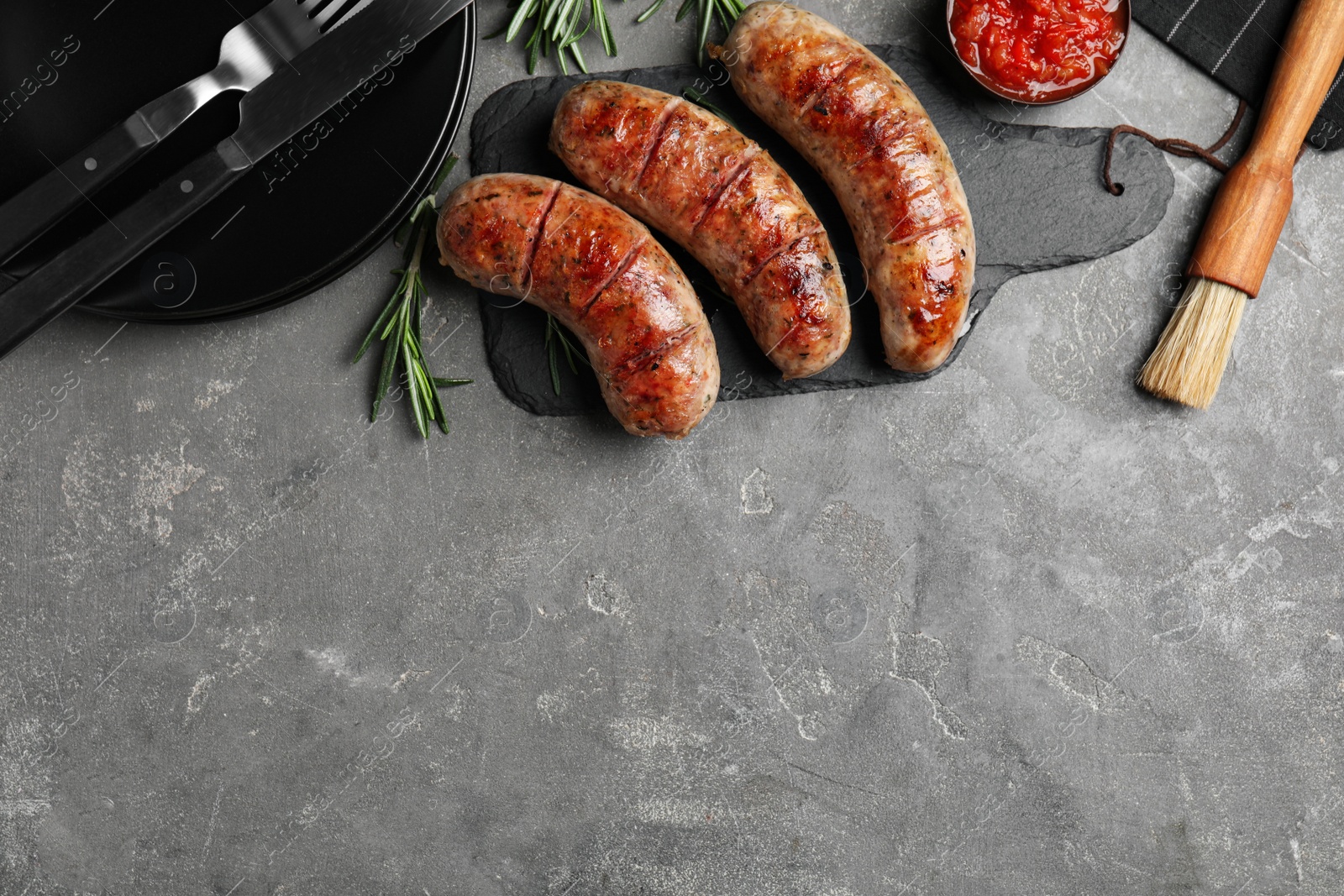 Photo of Tasty grilled sausages served on grey table, flat lay. Space for text