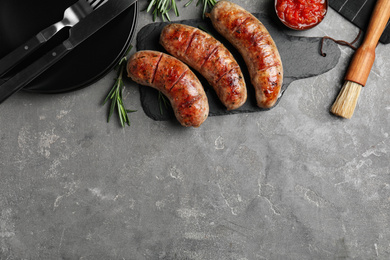 Tasty grilled sausages served on grey table, flat lay. Space for text