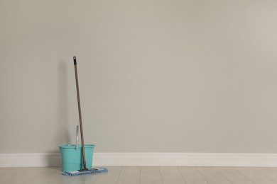 Mop and bucket on wooden floor near light grey wall, space for text. Cleaning service
