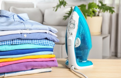 Photo of Stack of clean clothes and iron on table