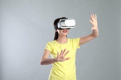 Photo of Woman using virtual reality headset on grey background