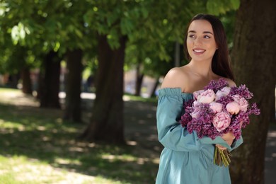 Photo of Beautiful woman with bouquet of spring flowers in park on sunny day, space for text