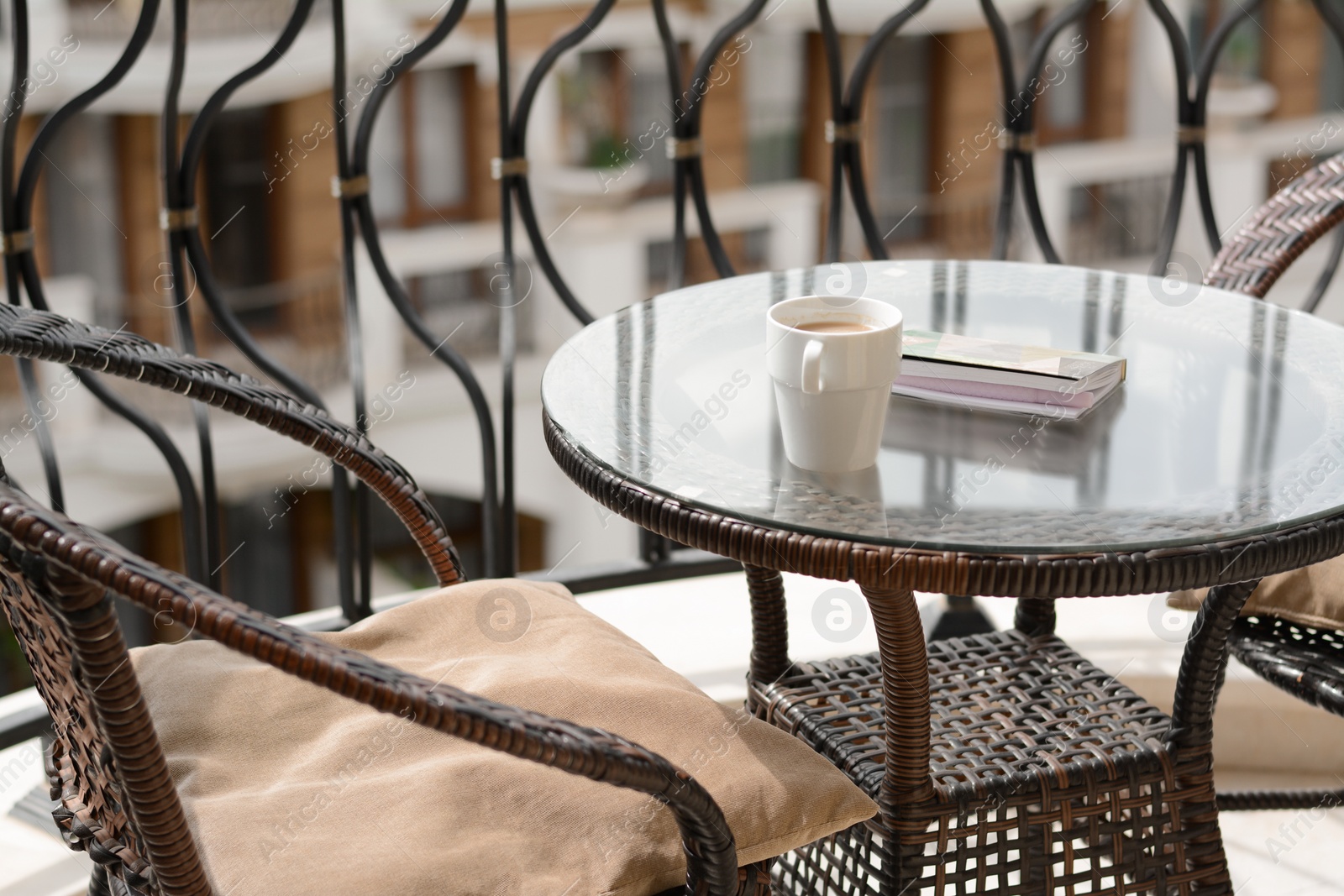 Photo of Stylish table with cup of coffee and notebook near comfortable armchair on balcony. Good morning