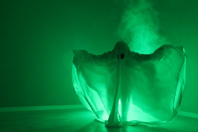 Creepy ghost. Woman covered with sheet in green light, space for text