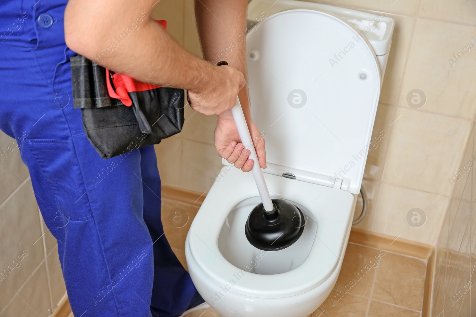 Photo of Plumber repairing toilet with hand plunger indoors