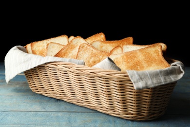 Photo of Slices of toasted bread in basket on light blue wooden table against black background