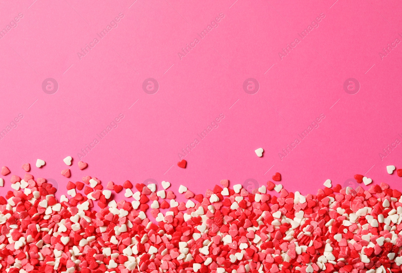 Photo of Heart shaped sprinkles on pink background, flat lay. Space for text