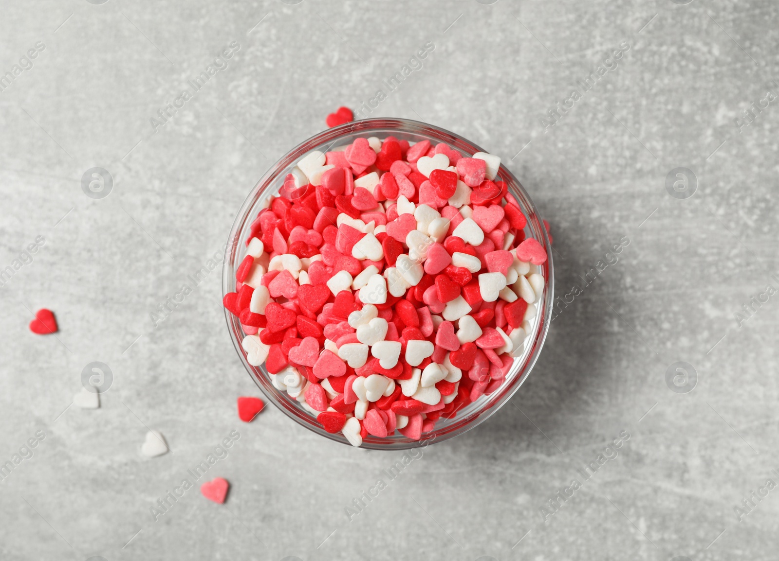 Photo of Bright heart shaped sprinkles in glass bowl on grey table, flat lay