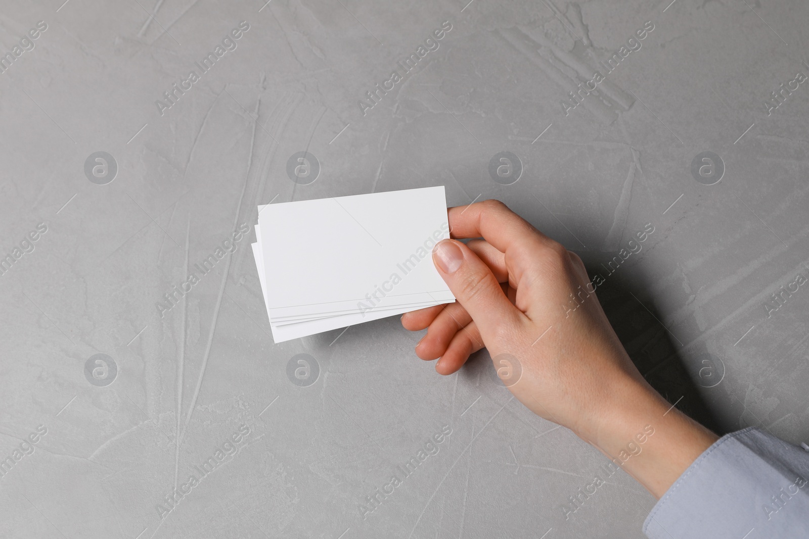 Photo of Woman holding blank cards at light grey table, top view. Mockup for design