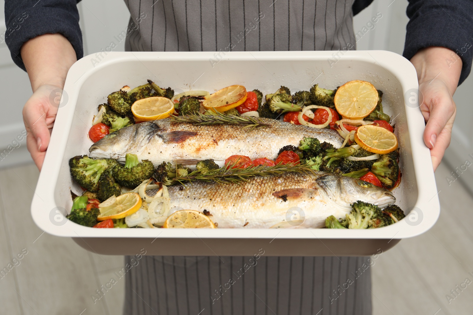 Photo of Woman holding baking dish with delicious fish and vegetables indoors, closeup