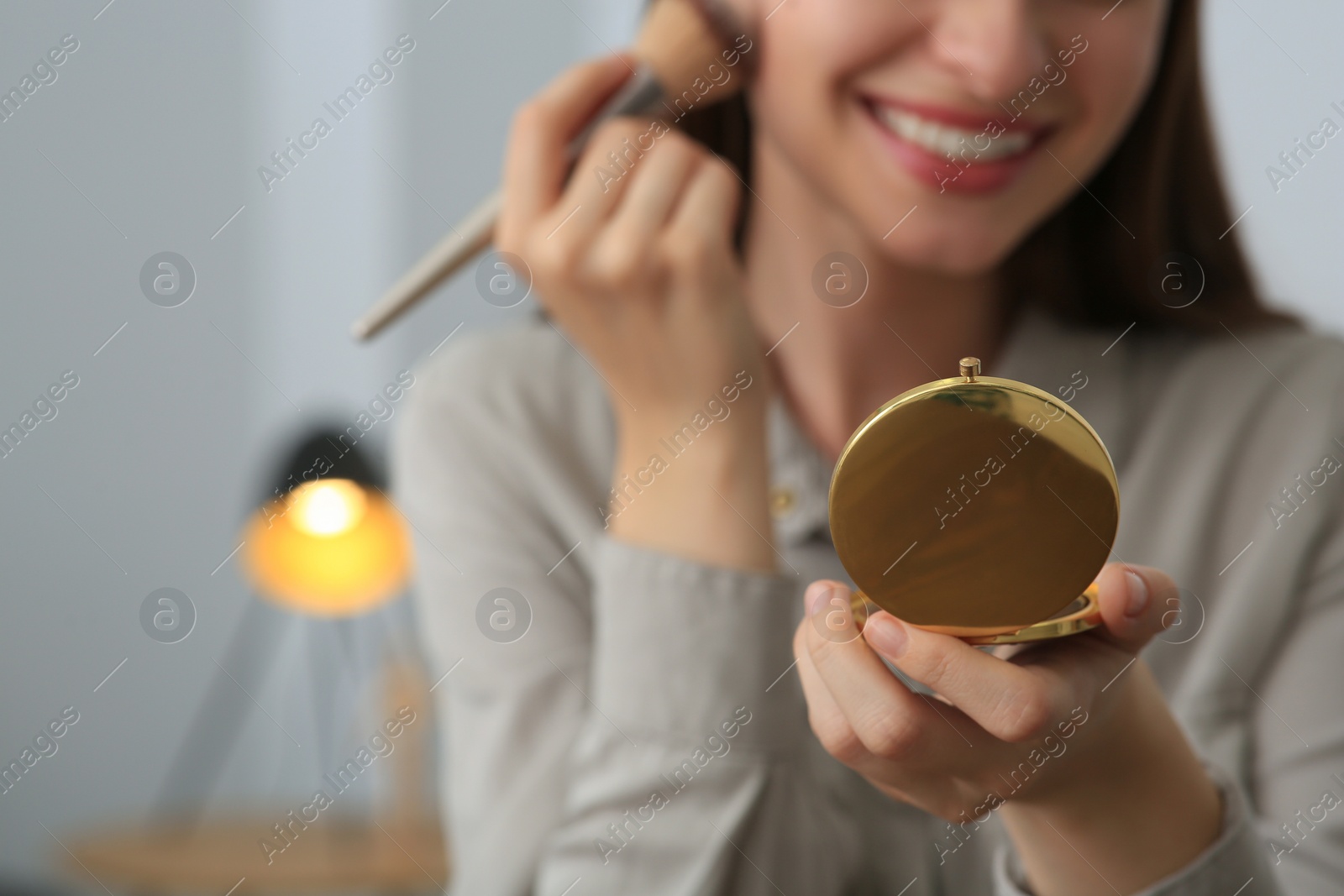 Photo of Young woman with cosmetic pocket mirror doing makeup indoors, closeup