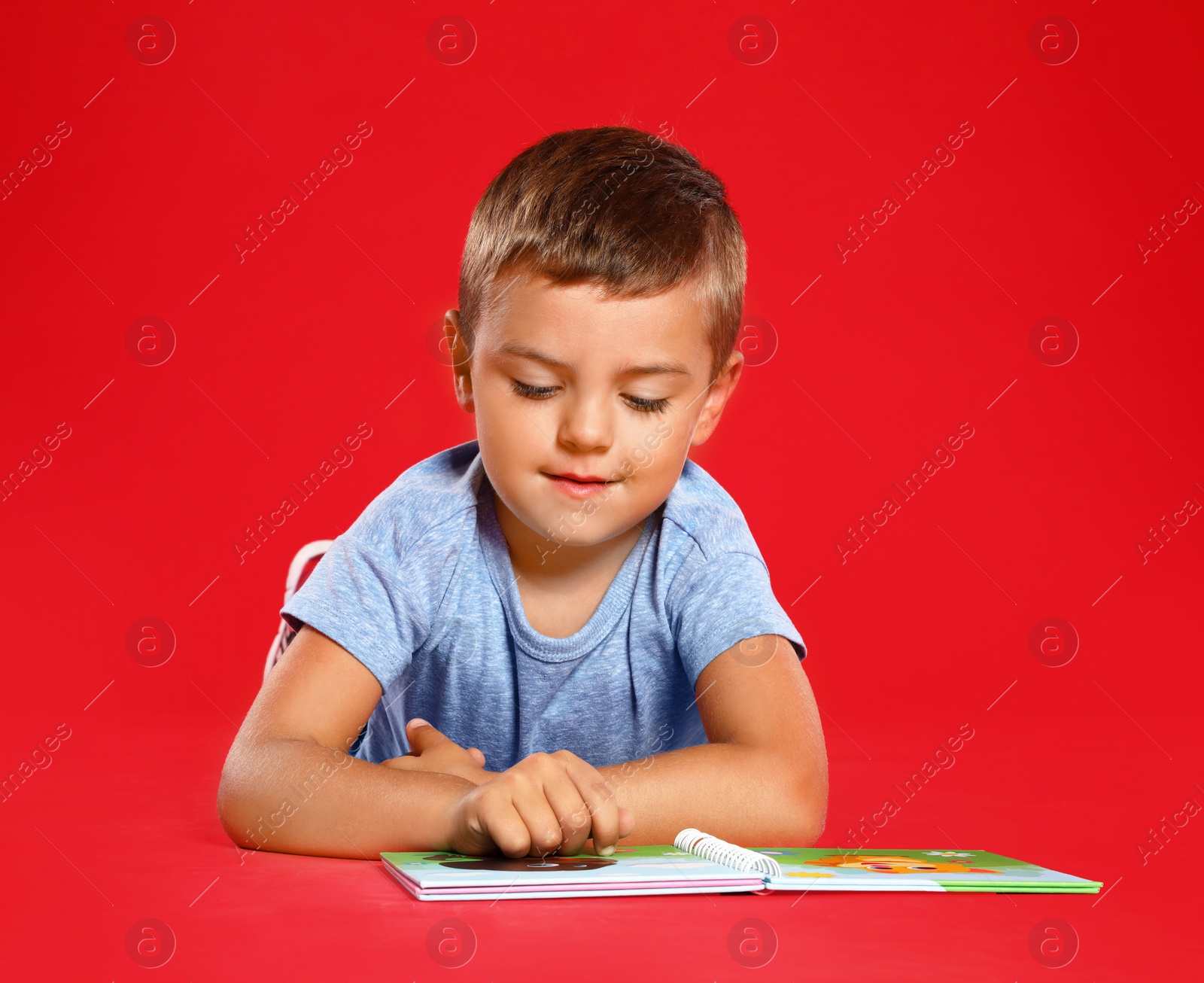 Photo of Cute little boy reading book on red background