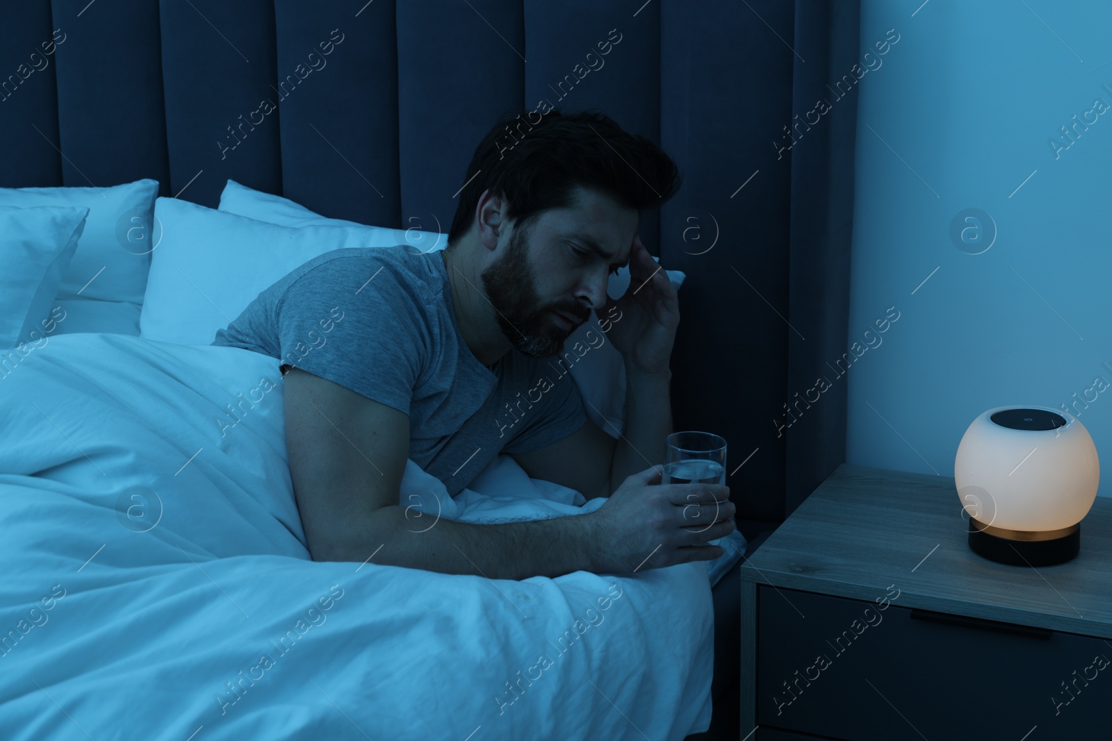 Photo of Man with glass of water suffering from headache in bed at night