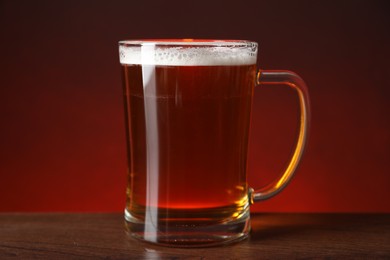 Mug with fresh beer on wooden table against color background, closeup