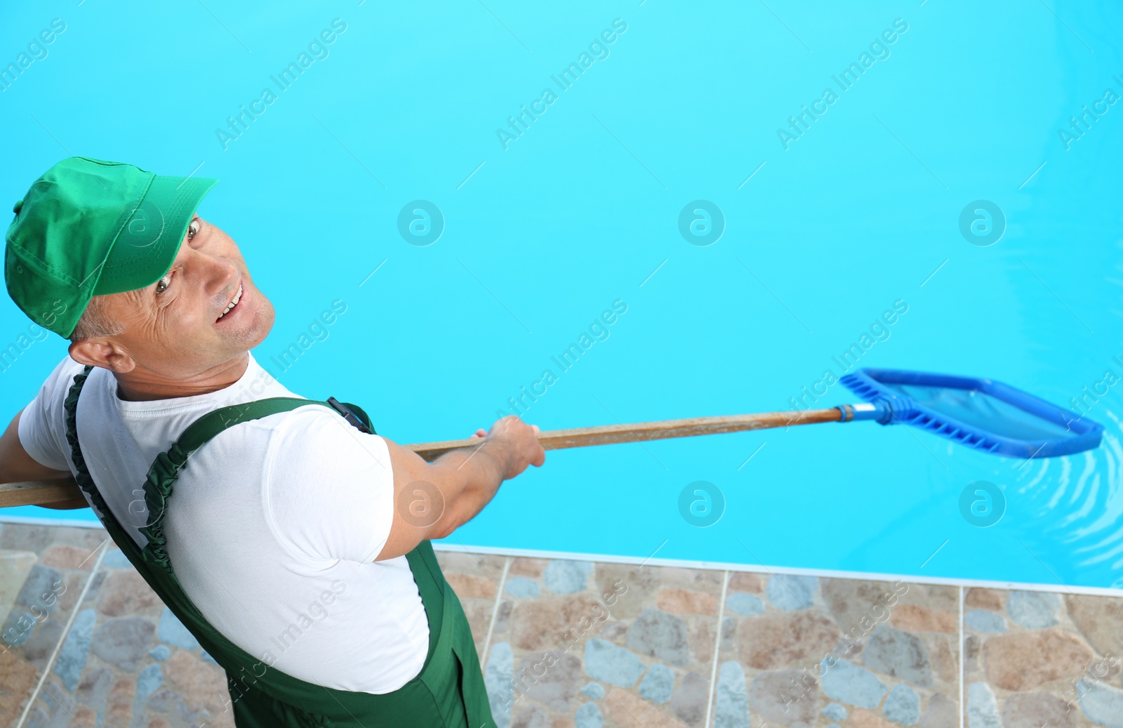 Photo of Male worker cleaning outdoor pool with scoop net