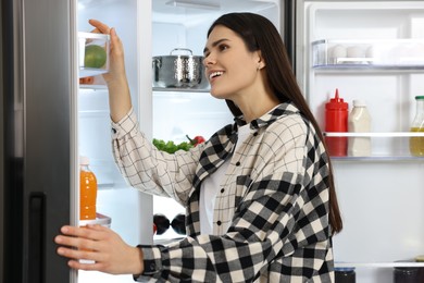 Young smiling woman looking into modern refrigerator