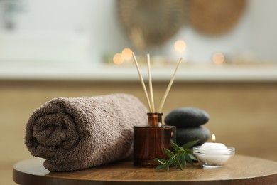 Photo of Spa composition. Rolled towel, aroma diffuser, massage stones and burning candle on wooden table indoors, closeup