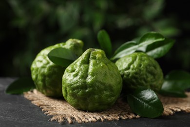 Photo of Fresh ripe bergamot fruits with green leaves on black table against blurred background, closeup