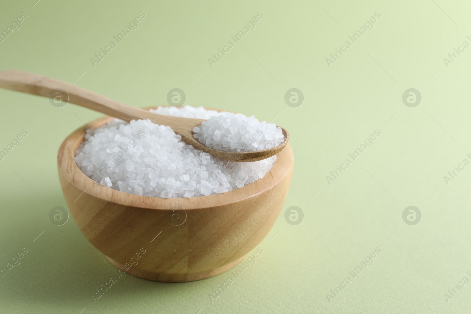 Photo of Organic white salt in bowl and spoon on olive background, space for text