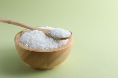 Photo of Organic white salt in bowl and spoon on olive background, space for text