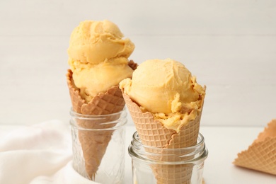 Photo of Delicious yellow ice cream in wafer cones and glass jars on table, closeup