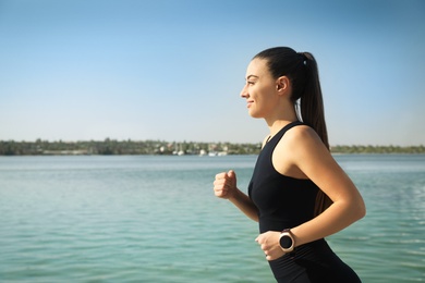 Photo of Woman wearing modern smart watch during training near river