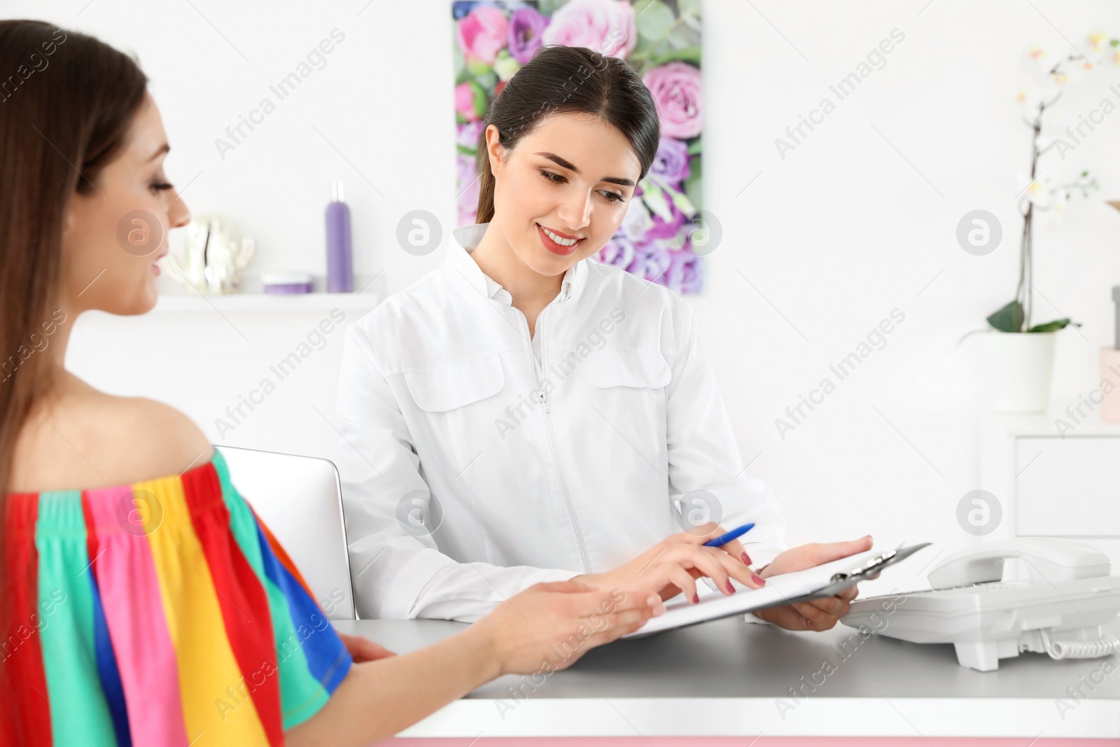 Photo of Young receptionist working with client at desk in beauty salon