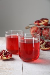 Photo of Tasty pomegranate juice in glasses and fresh fruits on white tiled table