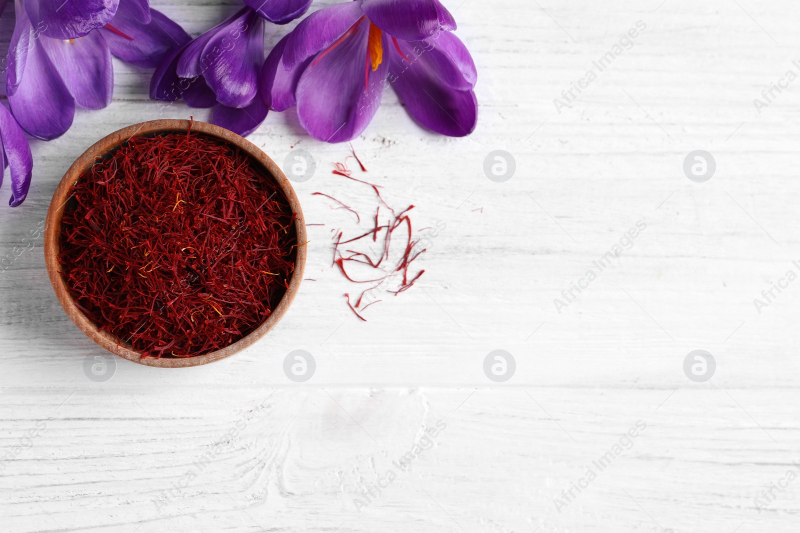 Photo of Dried saffron and crocus flowers on white wooden table, flat lay. Space for text