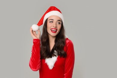 Photo of Christmas celebration. Beautiful young woman in red dress and Santa hat on grey background