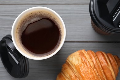 Photo of Coffee to go. Paper cups with tasty drink and croissant on grey wooden table, flat lay