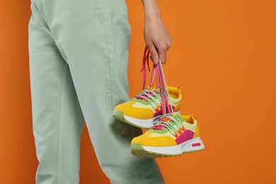 Photo of Woman holding pair of stylish colorful sneakers on orange background, closeup