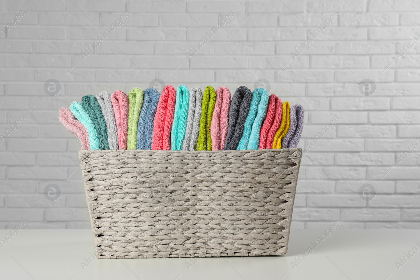 Photo of Wicker basket with folded towels on table near white brick wall