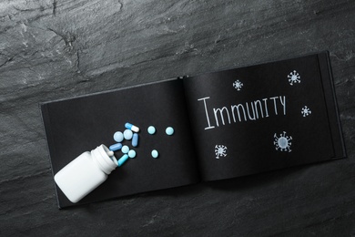 Notebook with word Immunity and pills on black table, top view