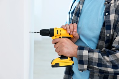 Photo of Young handyman working with electric drill at home, closeup