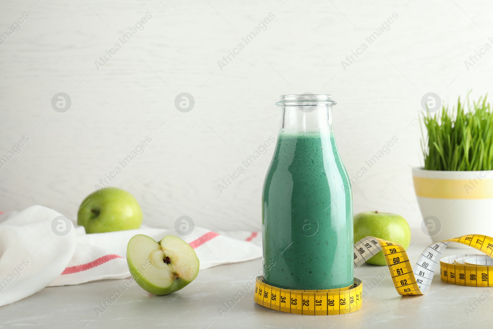 Photo of Composition with bottle of spirulina smoothie, measuring tape and apples on table. Space for text