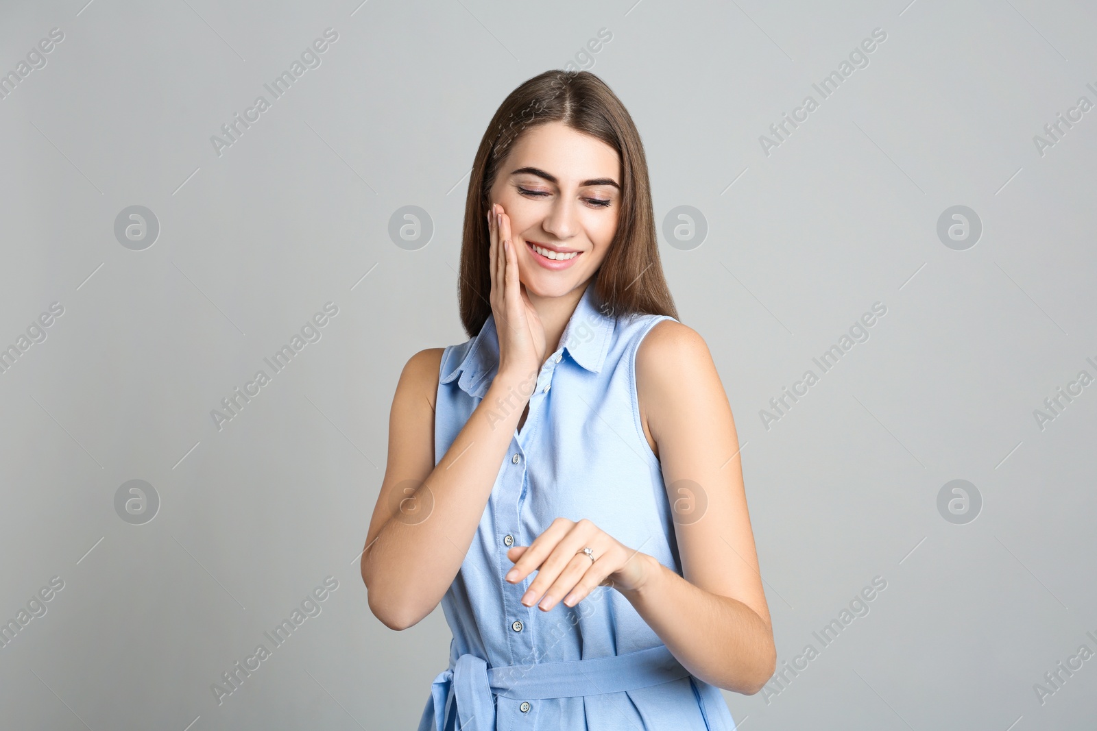 Photo of Happy young woman wearing beautiful engagement ring on grey background