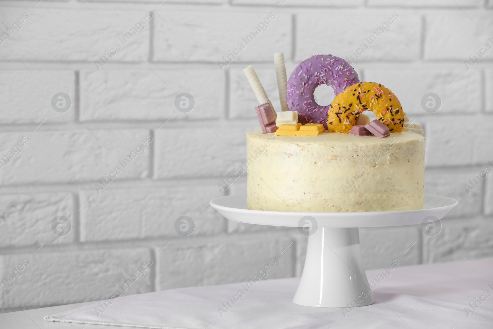 Photo of Delicious cake decorated with sweets on table near white brick wall, space for text