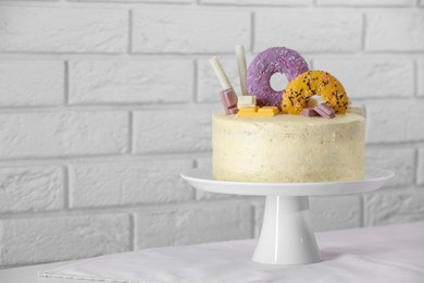 Photo of Delicious cake decorated with sweets on table near white brick wall, space for text