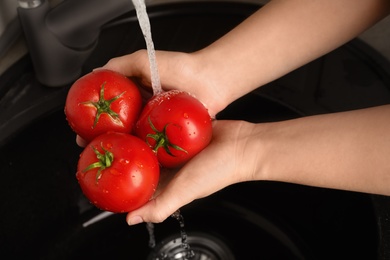 Photo of Woman washing ripe tomatoes in sink, closeup